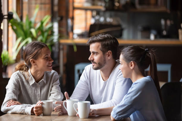 Diverse friends chatting, drinking coffee, sitting together in cafe