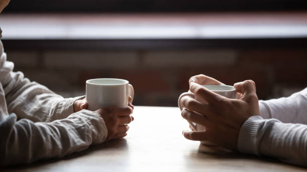 Close up woman and man holding cups of coffee on table Close up woman and man sitting in cafe, holding warm cups of coffee on table, young couple spending weekend in cozy coffeehouse together, romantic date concept, visitors drinking hot beverages cup of tea hands stock pictures, royalty-free photos & images