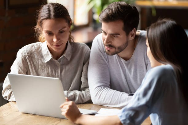 Real Estate Agent or insurance broker consulting young couple in cafe Real Estate Agent or insurance broker consulting young couple in cafe, sitting together at table, using laptop, looking at screen, financial advisor discussing mortgage or loan conditions with clients cafe racer stock pictures, royalty-free photos & images