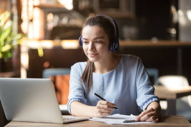 Focused woman wearing headphones using laptop, writing notes Focused woman wearing headphones using laptop in cafe, writing notes, attractive female student learning language, watching online webinar, listening audio course, e-learning education concept sports track stock pictures, royalty-free photos & images