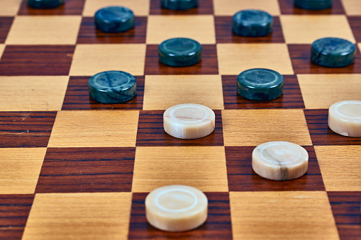 Malachite checkers and marble checkers on a wooden checkerboard. Close-up