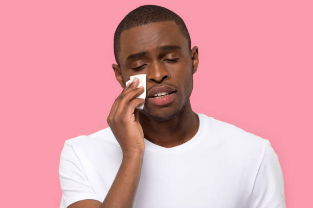 African male wiping tears feels unhappy posing over pink background Sad depressed african male holding paper tissue crying wiping tears feels unhappy posing over pink background isolated studio shot, broken heart personal problems sensitive person or break up concept wiping tears stock pictures, royalty-free photos & images