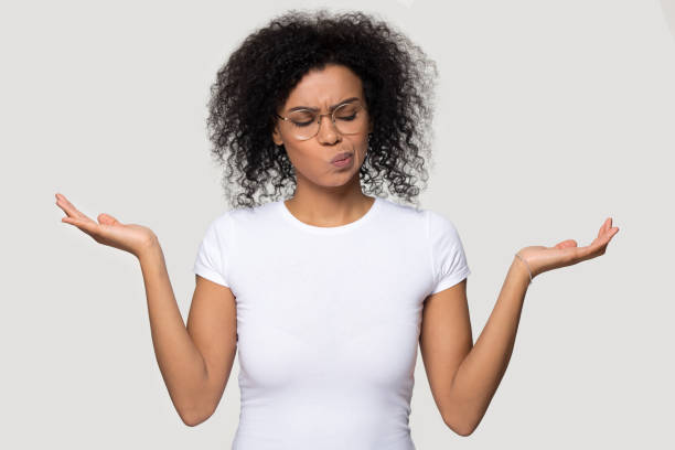 African woman on grey blank weigh the pros and cons African thoughtful woman in glasses white t-shirt stretched hands imagining alternatives weighs pros and cons isolated on grey blank background, concept of make important decision and choosing option pros and cons stock pictures, royalty-free photos & images