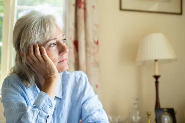 Senior Woman Suffering With Depression Looking Out Of Window At Home