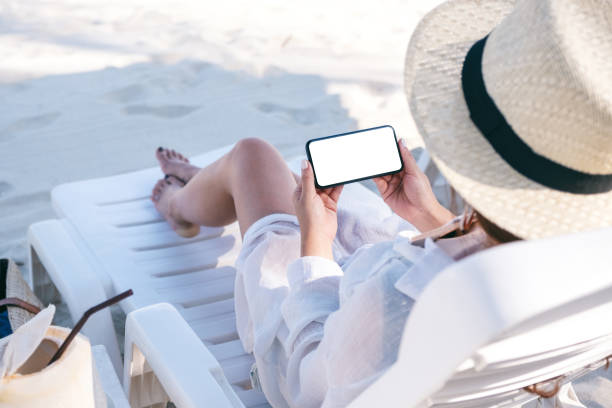 istock Mockup image of a woman holding black mobile phone with blank desktop screen while laying down on beach chair on the beach 1152791171