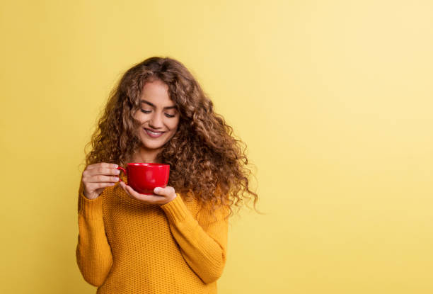 黄色の背景にスタジオで赤いカップと若い女性の肖像画。 - tea women cup drinking ストックフォトと画像