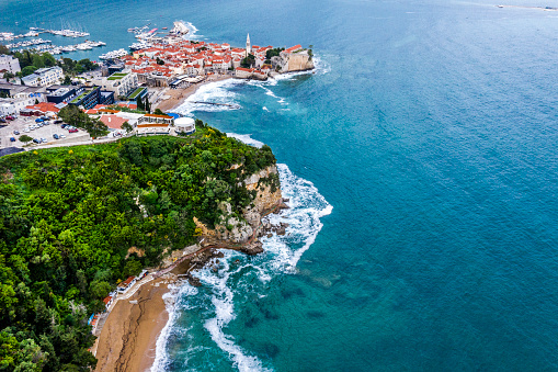 Wonderful high angle view of Budva on the edge of Adriatic sea, a hidden beach, lush forest and Old Town of Budva on top of old fort Mogren, captured by a drone.