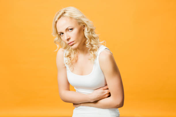 istock upset woman looking at camera while having stomach ache isolated on orange 1152795108