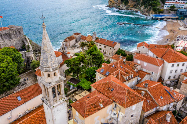 Aerial view of a Church bell tower rising from the rooftops of Old Town of Budva, situated on the Fortress Mogren Church bell tower dominating over the rooftop of Old Town of Budva, taken from air. rocky coastline stock pictures, royalty-free photos & images