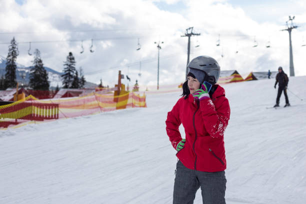 Woman snowboarder talking with friends on the phone at a ski resort. Woman snowboarder talking with friends on a smartphone while descending down the ski slope. bukovel ski resort ukraine stock pictures, royalty-free photos & images