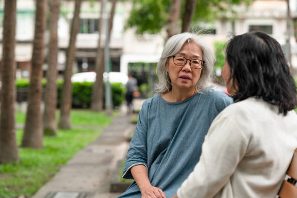 Two senior friends are spending time together in the park Two close senior friends are sitting on a park bench, spending time together talking about life and using social media. serious talk stock pictures, royalty-free photos & images