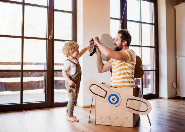 a toddler boy and father with carton plane playing indoors at home, flying concept. - glasses child cute offspring imagens e fotografias de stock