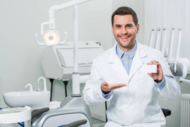 istock cheerful dentist in white coat smiling while showing blank card 1152817284