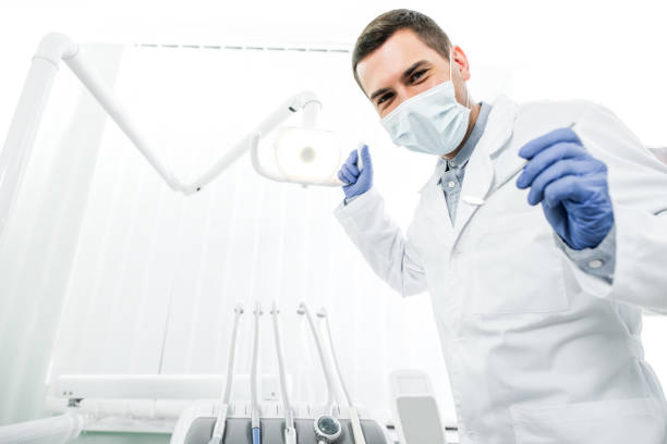 dentist in latex gloves and mask holding dental instrument and dental lamp stock photo