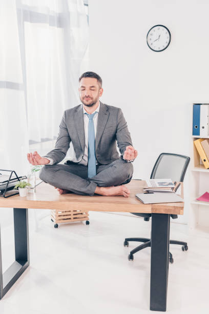 istock handsome businessman in suit meditating in Lotus Pose while sitting on office desk 1152818925