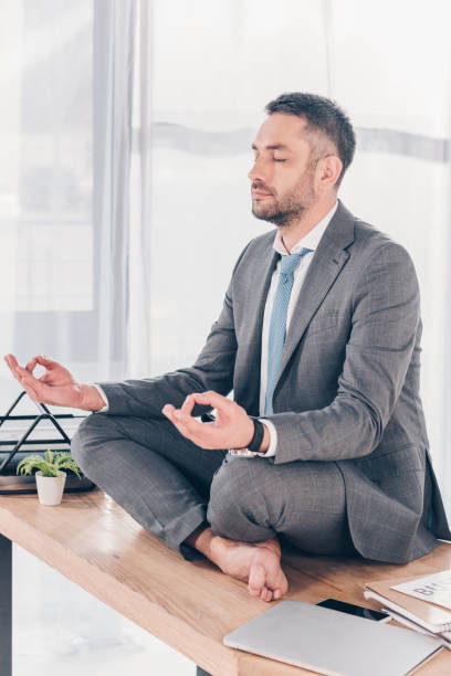 istock handsome businessman in suit meditating in Lotus Pose while sitting on office desk 1152818941