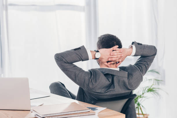 istock Back view of businessman with Hands Behind Back sitting at table in office 1152819119