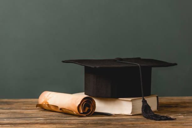 istock book, academic cap and scroll on wooden surface isolated on grey 1152821278