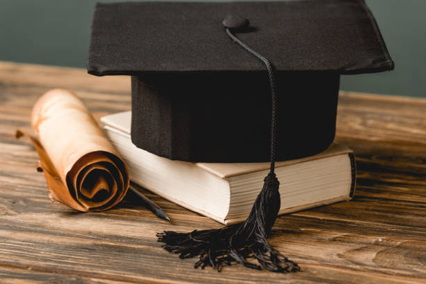 istock book, academic cap and scroll on wooden surface isolated on grey 1152821316