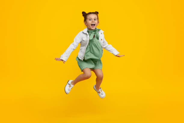 Trendy kid jumping and screaming Adorable little girl in stylish dress and jacket yelling and leaping up in excitement against bright yellow background jumping stock pictures, royalty-free photos & images
