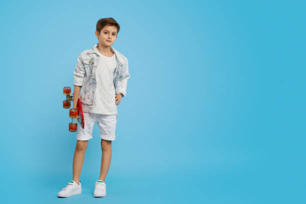 Confident trendy boy with skateboard Positive youngster with modern red longboard looking at camera while standing on empty blue background longboard skating photos stock pictures, royalty-free photos & images