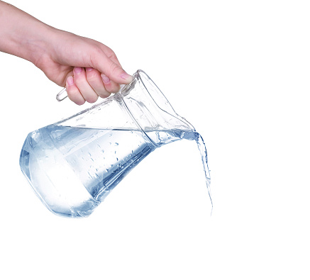 Pouring water from glass pitcher on white background