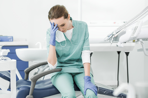 exhausted dentist holding head while sitting on chair in dental clinic
