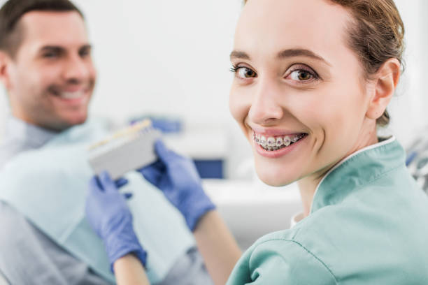 istock selective focus of cheerful dentist with braces on teeth smiling while holding color palette near patient 1152830225