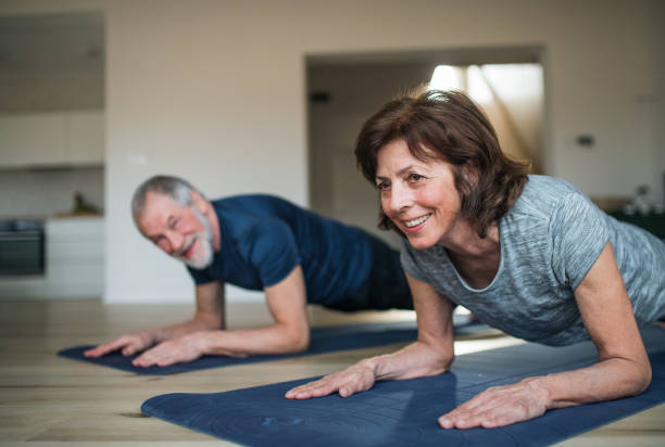 A senior couple indoors at home, doing exercise on the floor. A happy senior couple indoors at home, doing exercise on the floor. bodyweight training stock pictures, royalty-free photos & images