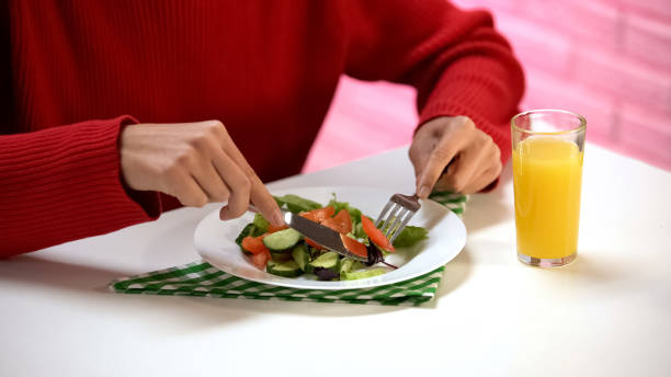istock Lady eating vegetable salad with fork and knife, fresh orange juice on table 1152830663