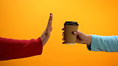 Lady showing stop gesture to paper cup on bright background, recycling problem