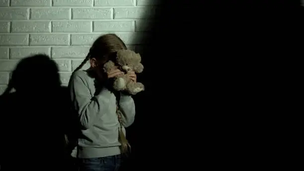 Scared girl covering eyes with teddy bear, ghost shadow on wall, nightmare