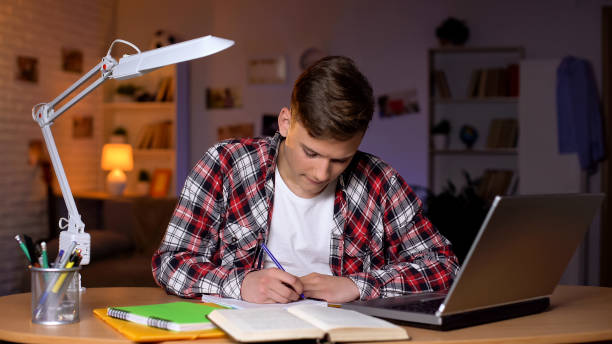 istock Teenager doing his homework, writing task into copybook, laptop on table 1152831160
