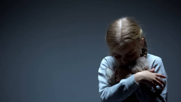 criança pequena só que abraça o urso de peluche, conceito do bullying, fundo escuro - dark little girls child happiness - fotografias e filmes do acervo