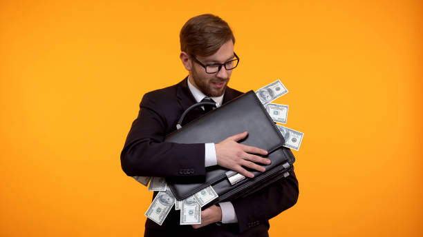 businessman holding briefcase full of money, isolated on yellow background - greed imagens e fotografias de stock