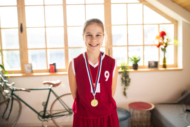 Portrait of cute, female,teenage basketball player in basketball uniform with medal around neck, smiling and looking at camera