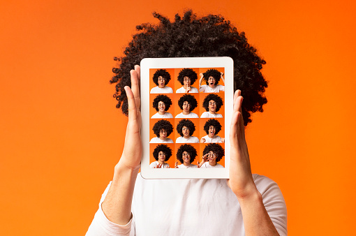 Concept of man choosing expression of face. Bushy guy hiding behind digital tablet with set of human emotions, orange background