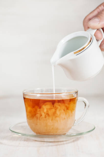 Milk poured into cup of tea by man hand stock photo