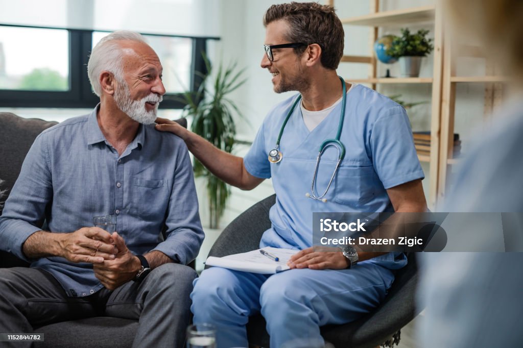 I'm glad to see you doing well! Happy doctor talking to senior male patient while being in a home visit. Doctor Stock Photo