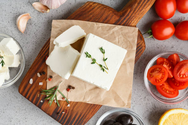 Homemade greek cheese concept Chopped feta on wooden board, herbs, olives and tomatoes on concrete background. Homemade greek cheese concept feta cheese block stock pictures, royalty-free photos & images