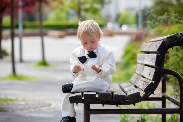 hermoso niño pequeño en esmoquin, jugando en un parque en un día de la boda - single lane road footpath flower formal garden fotografías e imágenes de stock