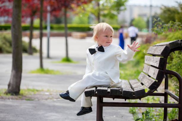 hermoso niño pequeño en esmoquin, jugando en un parque en un día de la boda - single lane road footpath flower formal garden fotografías e imágenes de stock