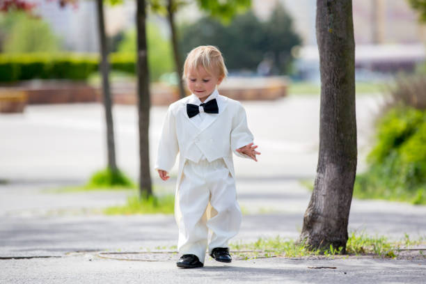 beau garçon d’enfant en smoking, jouant dans un parc sur un jour de mariage - baby toddler child flower photos et images de collection