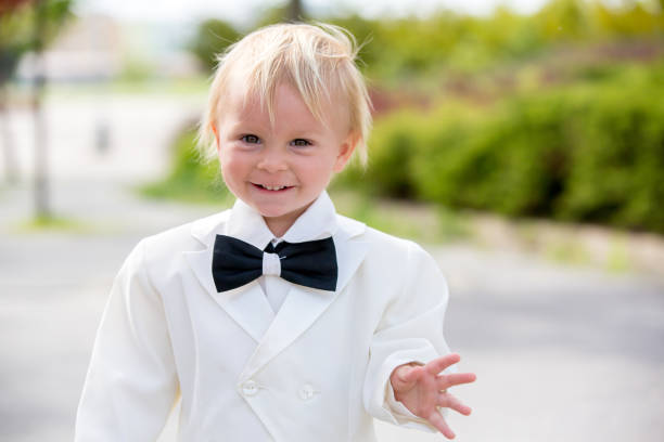 hermoso niño pequeño en esmoquin, jugando en un parque en un día de la boda - single lane road footpath flower formal garden fotografías e imágenes de stock