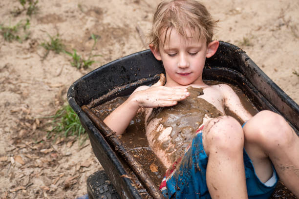 young boy playing in mud in wheelbarrow filled with water stock photo