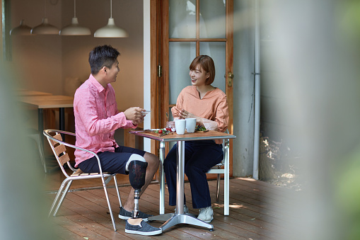 Happy woman and disable man talking at cafe. Heterosexual couple is wearing casuals while sitting. They are having meal at table.