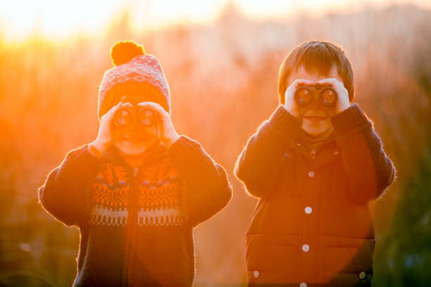 duas crianças pequenas, meninos, explorando a natureza com binóculos - searching landscape sunset winter - fotografias e filmes do acervo