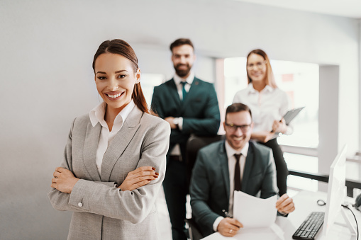 Portrait of handsome smiling businessman with his colleagues. Multi-ethnic group of business persons standing in modern office. Successful team leader and his team in background.