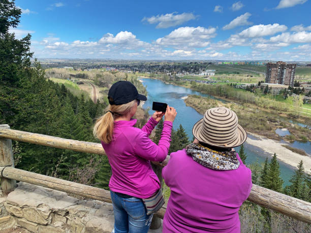 Photographing the view during a hike, Calgary,Canada Calgary,Canada - May 15, 2019: Rear view of two women taking pictures with a smartphone and a digital camera of  the Bow River and the surrounding landscape, while standing on the viewpoint at Edworthy Park, during a hike at the Douglas Fir Trail. iphone 8 stock pictures, royalty-free photos & images