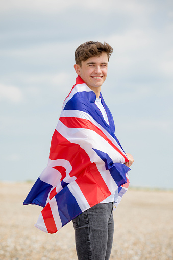 Young adult Caucasian male holding on a beach holding the flag of Great Britain